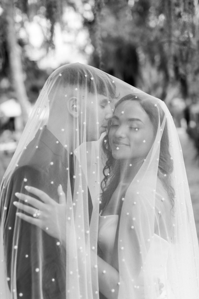 Black and white photo of bride and groom under wedding veil at Fountain of Youth wedding.