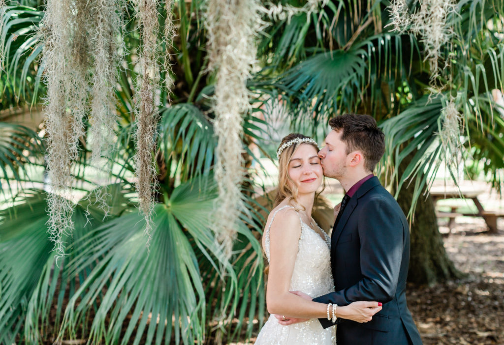 Groom kissing his bride under a palm tree. 